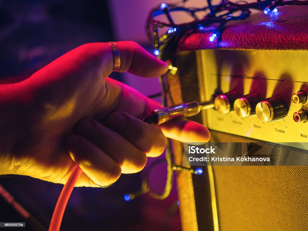 Man plugging jack into the guitar amplifier, closeup, for music, entertainment themes. Neon colorful light Amplifier Stock Photo