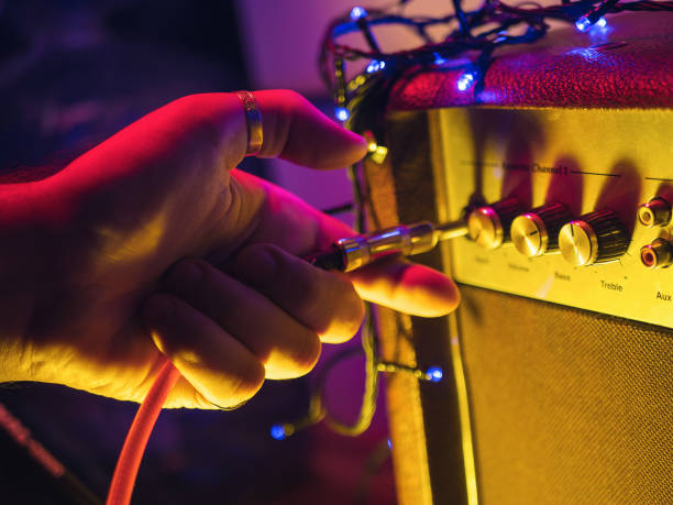 Man plugging jack into the guitar amplifier, closeup, for music, entertainment themes. Neon colorful light Man plugging jack into the guitar amplifier, closeup, for music, entertainment themes. Neon colorful light loudon stock pictures, royalty-free photos & images