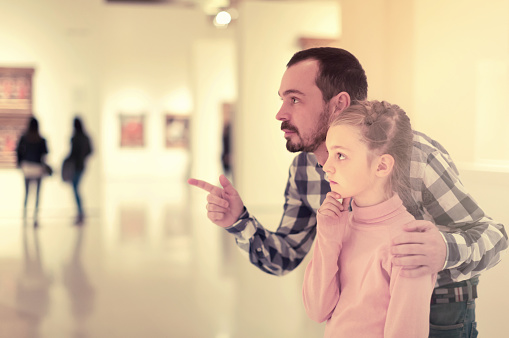Young father and girl exploring paintings in halls of museum