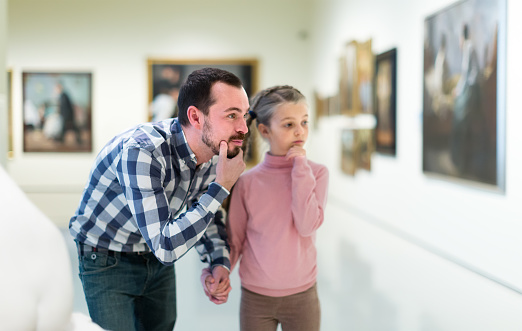 interested father and daughter regarding paintings in halls of museum
