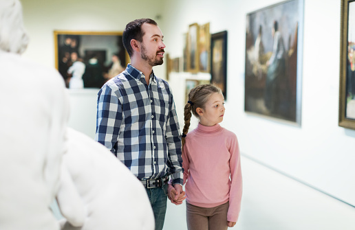 Glad young father and little daughter looking at expositions in museum