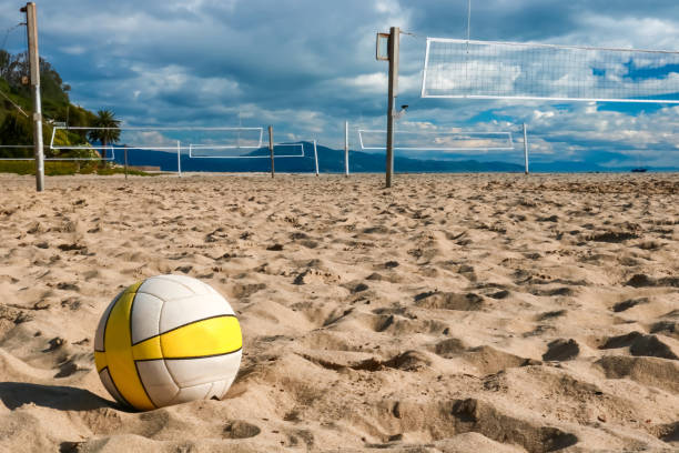 Volleyball in Close Foreground Sits on Beach with Nets and Courts Beyond Volleyball in foreground with empty courts and nets on sandy beach beyond. beach volleyball stock pictures, royalty-free photos & images