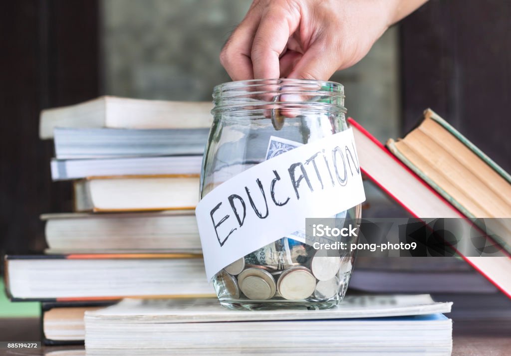 Coins and banknote in a glass jar placed on the textbook. Coins and banknote in a glass jar placed on the textbook. Concept money saving for education. Education Stock Photo