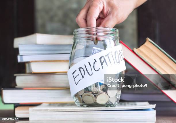 Coins And Banknote In A Glass Jar Placed On The Textbook Stock Photo - Download Image Now