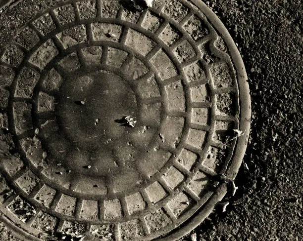 A very old manhole cover that has been considerably worn down by years of street traffic.