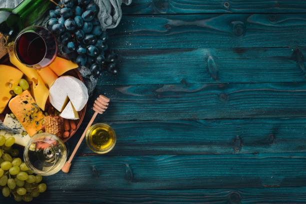 A large assortment of cheeses, wine, honey, nuts and spices, on a blue wooden table. Top view. Free space for text.