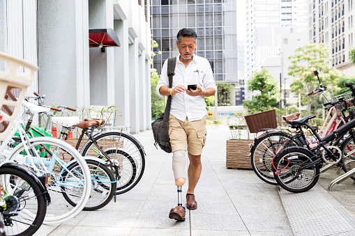 Hombre japonés con prótesis pierna caminando por el estacionamiento mientras revisa su teléfono photo