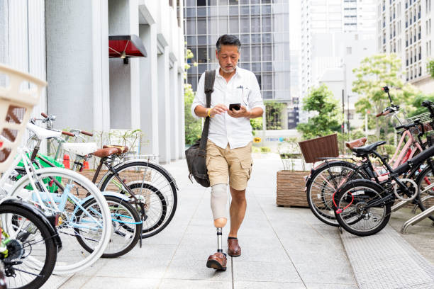 homem japonês com perna protética andando no estacionamento durante a verificação de seu telefone - rush hour commuter on the phone tokyo prefecture - fotografias e filmes do acervo