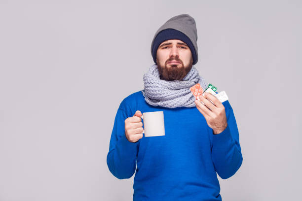 Sick bearded man holding cup with tea, many pills. Sick bearded man holding cup with tea, many pills. Studio shot, isolated on gray background sneezeweed stock pictures, royalty-free photos & images