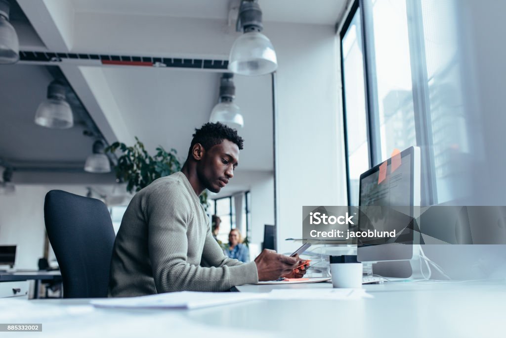 Male executive using mobile phone in office Male executive sitting in work place and using mobile phone. Young businessman working in office. Working Stock Photo