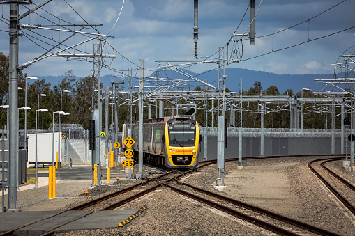 Redcliffe, Australia – November 20, 2017: Queensland Rail commuter train emerges from razor-wire security fence surrounding railway storage yard.  Cross-over junction leads to Kippa-Ring station terminus.