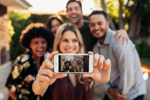 Joyful friends taking selfie during outdoor party Happy young friends having fun at party taking selfie. Focus on mobile phone in hands of female. selfie photos stock pictures, royalty-free photos & images