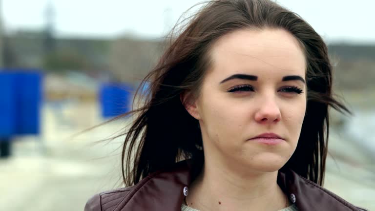 Portrait of a young beautiful girl with long brown hair. The girl straightens her hair and laughs and chewing chewing gum. A cloudy autumn day on the beach.