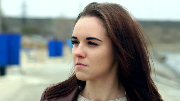 Portrait of a young beautiful girl with long brown hair. The girl straightens her hair and laughs and chewing chewing gum. A cloudy autumn day on the beach.