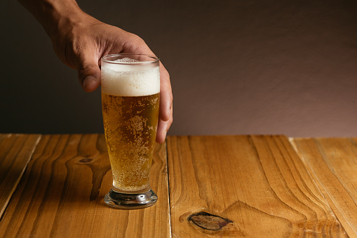 Close up of a male hand taking a glass of beer from wood table