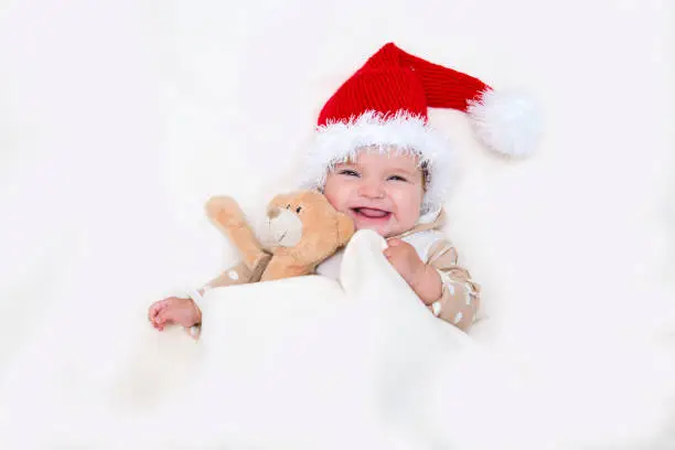 Photo of The cheerful Christmas baby to a Santa hat and Teddie's bear