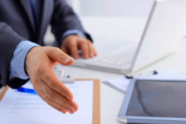 istock Man wearing a suit offering to shake hands, sitting on desk 885436178