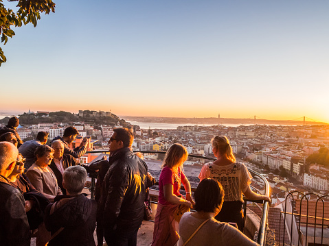 Lisbon, Portugal - November 19, 2017: Tourists at Belvedere of Our Lady of the Hill viewpoint, looking at the cityscape of Lisbon at sunset.
