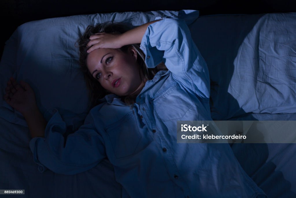 Sleep disorder, insomnia. Young blonde woman lying on the bed awake Insomnia Stock Photo