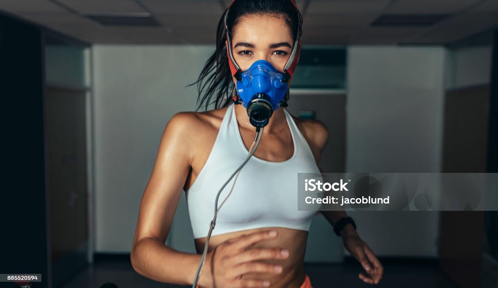 Sportswoman with mask running on treadmill in gym Portrait of sportswoman with mask running on treadmill in gym. Female athlete in sports science lab measuring her performance. Medical Exam Stock Photo