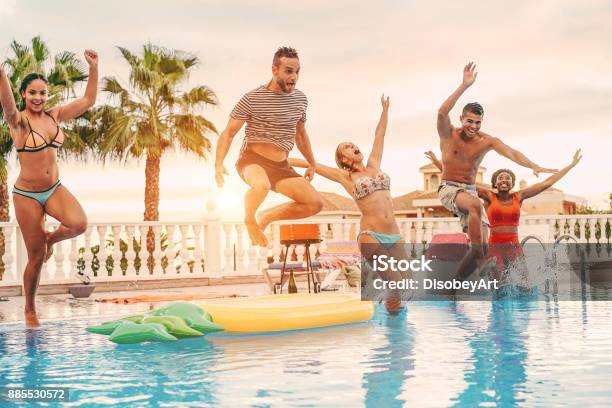 Group Of Happy Friends Drinking Jumping In Pool Sunset Party Outdoor Young Diverse Culture People Having Fun In Tropical Vacation Holiday Youth And Friendship Concept Main Focus On Left Man Stock Photo - Download Image Now