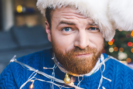 close-up portrait of bearded man in santa hat tied up with christmas garland