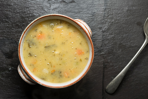 Rustic bowl of vegetable soup on a dark grey slate background.