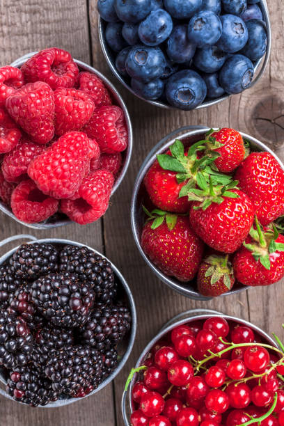 istock Berries closeup assortment in tin cans overhead on wooden table 885542128