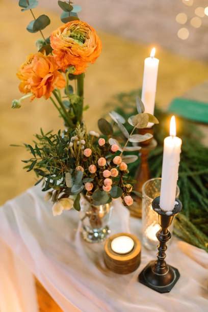 istock feast, present, floral design concept. on thick drapping two small extremely beautiful posies with bright orange roses, lots of various leaves and small light pink berries, they are placed by candles 885542366