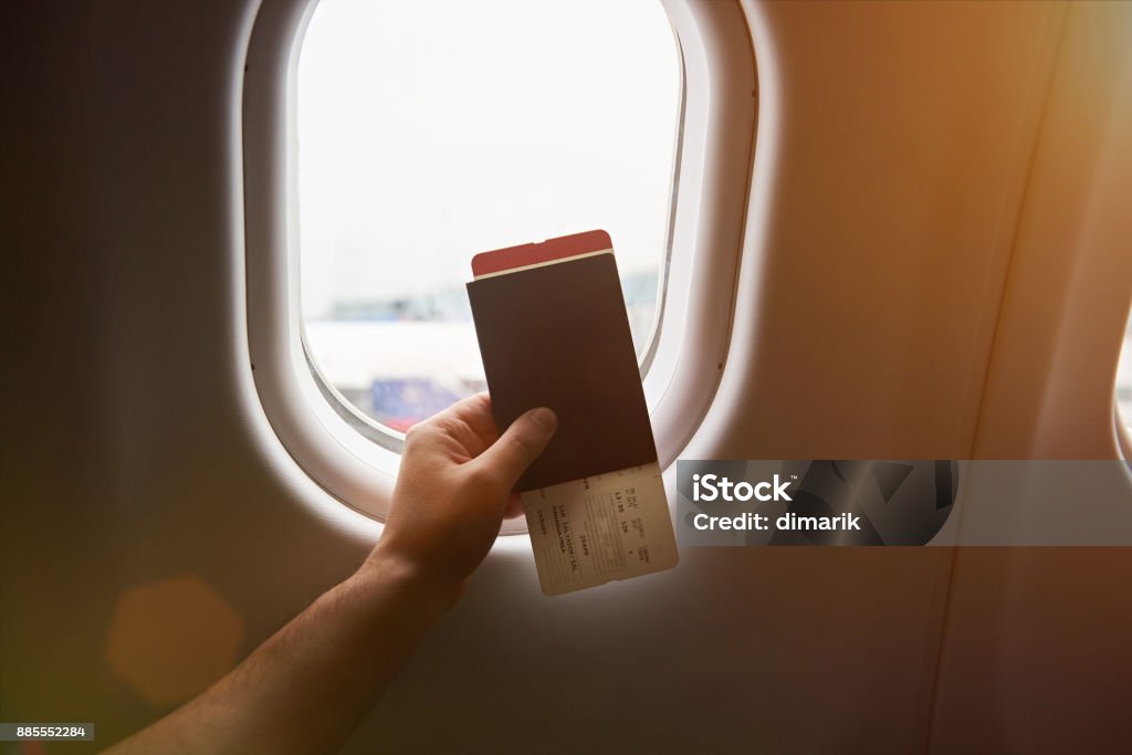 Hand holding passport Hand holding passport with airplane ticket on plane window sunny background Airplane Ticket Stock Photo