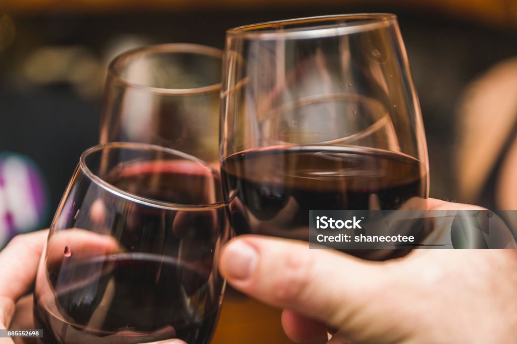 Three Wine Glasses Touching Three people touch their drinks together in a "cheers" tradition of clinking glasses together in a social situation with alcohol. Pinot Noir Grape Stock Photo