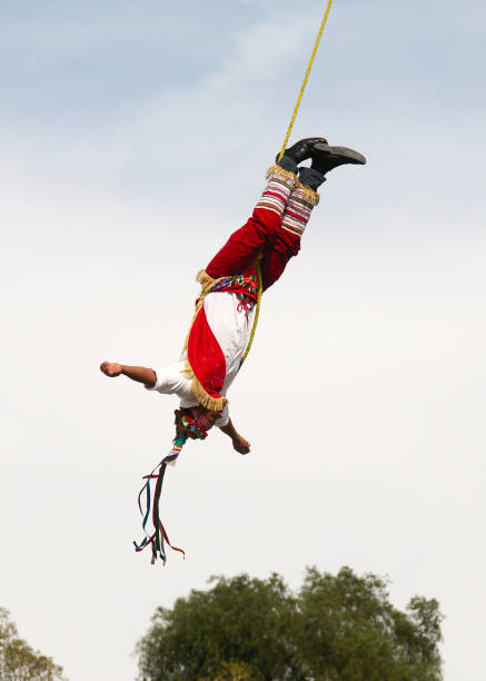 The Acrobat Flyers Cholula, Puebla, Mexico - 2017: A member of the acrobats known as "los voladores" performs in front of the Great Pyramid of Cholula and Nuestra Señora de los Remedios church. volador stock pictures, royalty-free photos & images