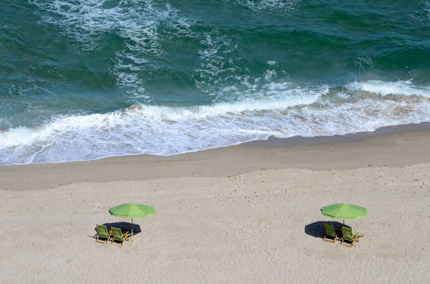 Overhead view of the waves and surf of the Atlantic Ocean rolling into the beach in front of a beach umbrella and lounge chairs at Singer Island in West Palm Beach, Florida. Taken just after sunrise with amazing light on the sand and water.