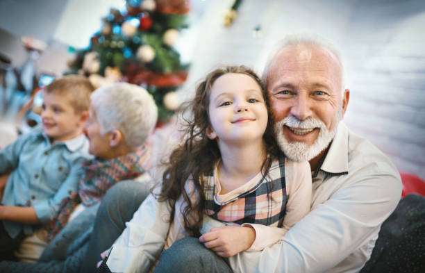Senior couple playing with grandchildren. Closeup of senior couple spending some quality time with their grandchildren on Christmas eve. They are sitting on a sofa and enjoying playing with kids. Grandfather and little girl are looking at the camera. multi generation family christmas stock pictures, royalty-free photos & images