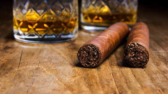 Dos puros cubanos con dos vasos de whisky en una vieja mesa de madera con un fondo borroso photo