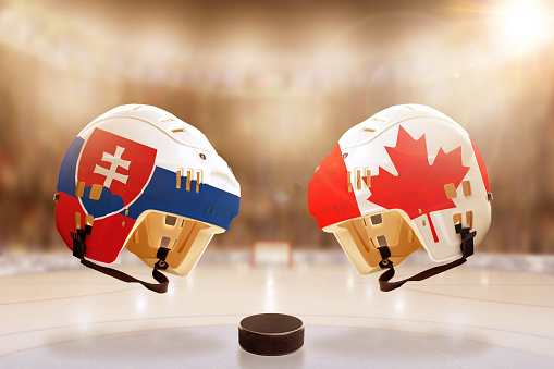 Low angle view of hockey helmets with Canada and Slovakia flags painted and hockey puck on ice in brightly lit stadium background. Concept of intense rivalry between the two hockey nations. Fictitious arena created in Photoshop.