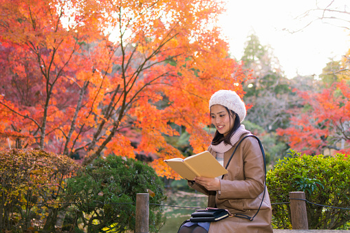 Young woman reading book under autumn foliage