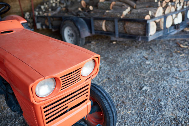 High-angle view of an orange tractor next to a trail loaded with a stack of logs at farm in the countryside