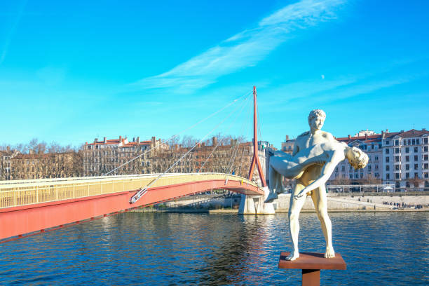 Lyon,  France - December 8, 2016: The Weight of Oneself sculpture by Michael Elmgreen, on the Soane river bank, with the Palais de Justice footbridge in the background