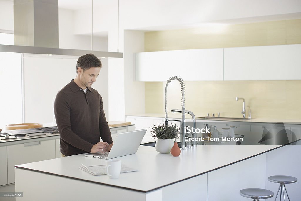 Homme utilisant un ordinateur portable dans la cuisine - Photo de 30-34 ans libre de droits