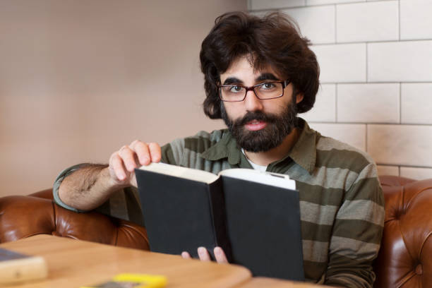 istock Photo handsome bearded man wearing glasses reading book 885838526