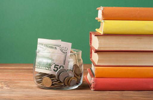 Coins in glass jar and stack of books on wooden table.Concept of funding education.