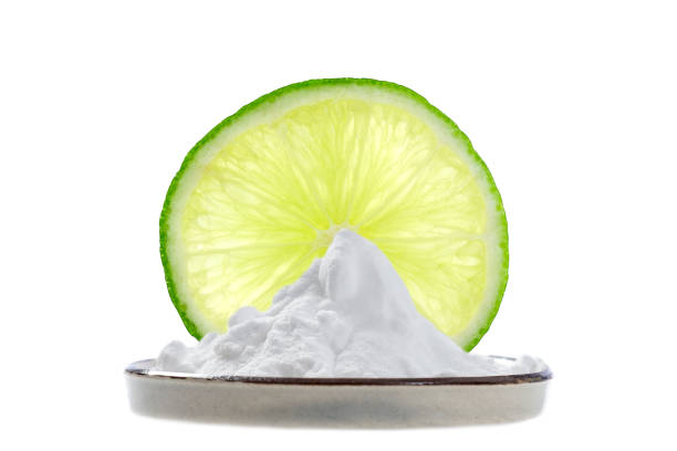 sodium bicarbonate in a cup with a fine slice of lemon and two whole lime behind stock photo
