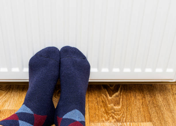 istock Person's feet in woolen socks warming them against an heating radiator. Copy-space. 885953384