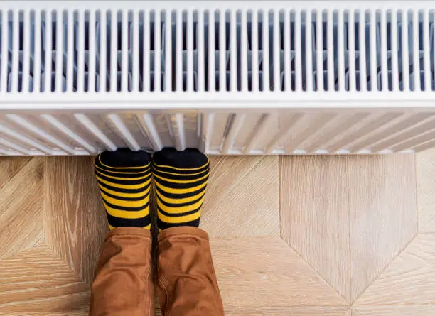 Person's feet in bright yellow-black socks warming them against an heating radiator. Copy-space.