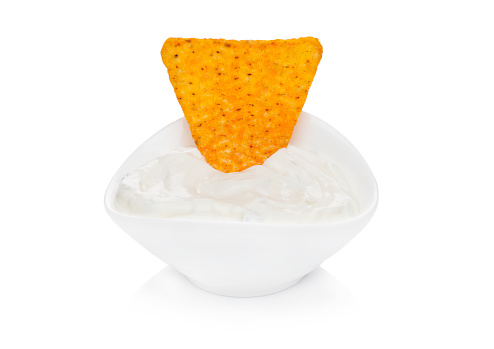 Glass container with sour cream dip and nachos chips on white background