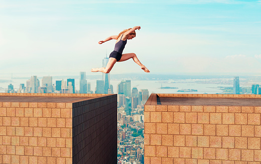 Female with bare feet runs and jumps from one tall building to another. She looks down as she is right a above the gap between the buildings. Big city in the background with skyscapers. Concept of taking a change even though there is a big risk.