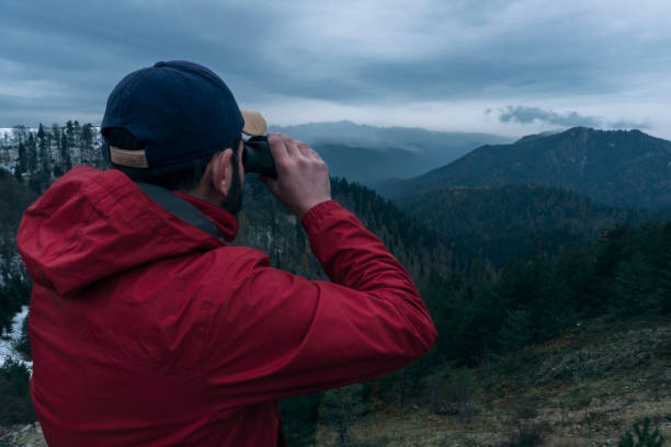 istock Young man standing on the mountain peak and looking through binoculars 885970980