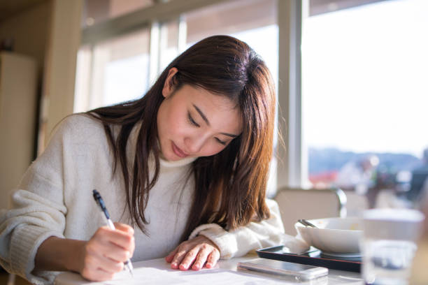 Young woman writing document nearby window