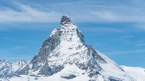 Iconic view of Snowy Matterhorn peak with blue sky and some clouds in background, Switzerland